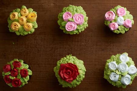 cupcake decorated with chantilly with rose design, placed on a wooden base, diffuse background of more cupcakeの写真素材