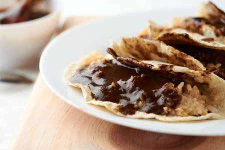 Tacos of mole with rice, placed on wood, in the background a piece of chickenの写真素材