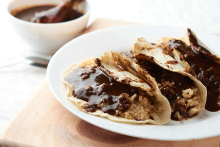Tacos of mole with rice, placed on wood, in the background a piece of chickenの写真素材