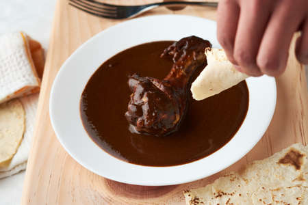 Chicken with mole, person taking a piece of tortilla, Mexican tradition, placed on woodの写真素材