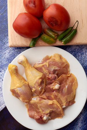 Chicken pieces placed on a plate, garnish tomatoes and chili peppers placed on a wood.の写真素材