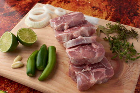 Pork for tacos, knuckle, around there are serrano peppers, garlic, onion, oregano, thyme and bay leaves, lemon, placed on a wooden base.の写真素材
