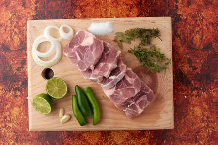 Pork for tacos, knuckle, around there are serrano peppers, garlic, onion, oregano, thyme and bay leaves, lemon, placed on a wooden base.の写真素材