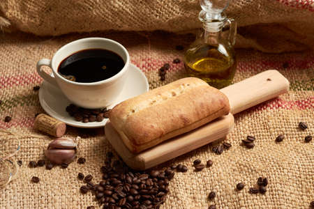 Rustic bread placed on a cutting board, around it a cup of American-style coffee, olive oil, coffee beans and garlic, placed in a vegetable fiber sackの写真素材