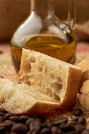 Rustic bread placed on a cutting board, around it a cup of American-style coffee, olive oil, coffee beans and garlic, placed in a vegetable fiber sackの写真素材