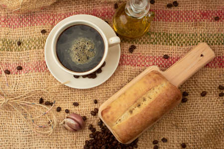 Rustic bread placed on a cutting board, around it a cup of American-style coffee, olive oil, coffee...