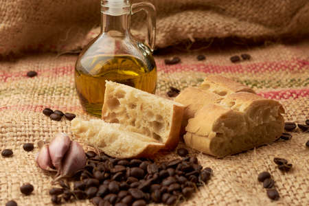 piece of rustic bread, around it coffee beans, olive oil, garlic, placed in a vegetable fiber sackの写真素材