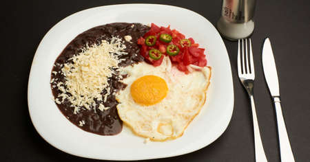 Fried egg accompanied with tomato and sliced jalapeÃ±o pepper, beans with grated cheeseの写真素材