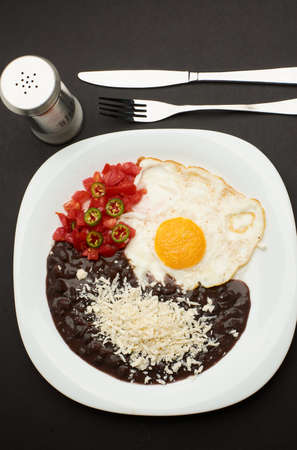 Fried egg accompanied with tomato and sliced jalapeÃ±o pepper, beans with grated cheeseの写真素材