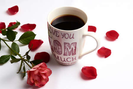 Cup of Americano type coffee, with the legend on the cup "I love you very much mom", adorned with a rose and petals aroundの写真素材