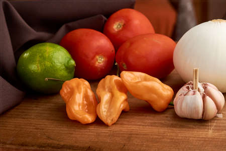 Yellow habanero chili, red tomatoes and white onion all placed on a wooden baseの写真素材