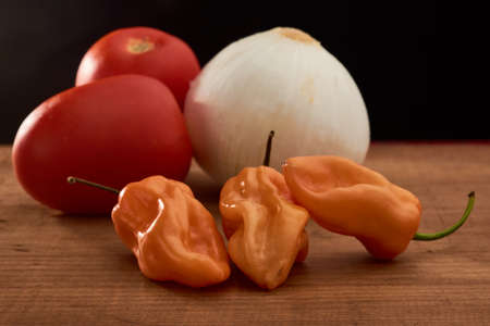 Yellow habanero chili, red tomatoes and white onion all placed on a wooden baseの写真素材