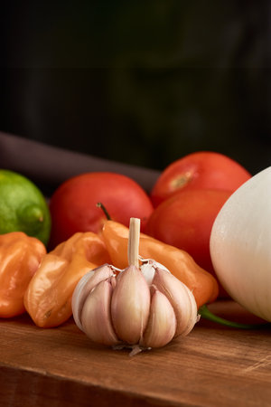 Garlic, yellow habanero chili, red tomatoes and white onion all placed on a wooden baseの写真素材