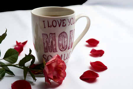 Cup of Americano type coffee, with the legend on the cup "I love you very much mom", adorned with a rose and petals aroundの写真素材