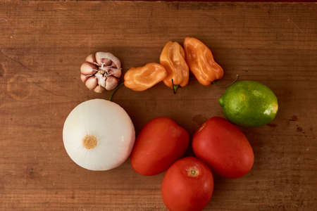 Yellow habanero chili, red tomatoes and white onion all placed on a wooden baseの写真素材