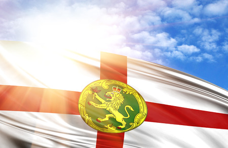 flag of Alderney against the blue sky with sun rays.