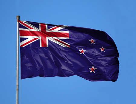 National flag of New Zealand on a flagpole in front of blue sky.の写真素材