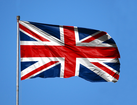 National flag of United Kingdom on a flagpole in front of blue sky.