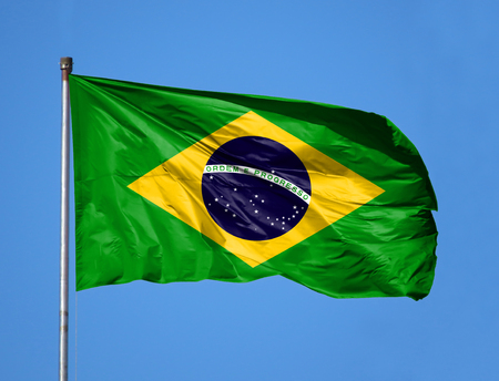 National flag of Brazil on a flagpole in front of blue sky.の写真素材