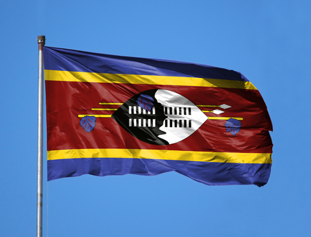 National flag of Swaziland on a flagpole in front of blue sky.の写真素材