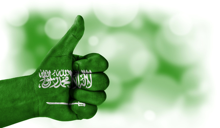 Flag of Saudi Arabia drawn on a man's hand with a thumb up, on a blurry background with a good place for textの写真素材