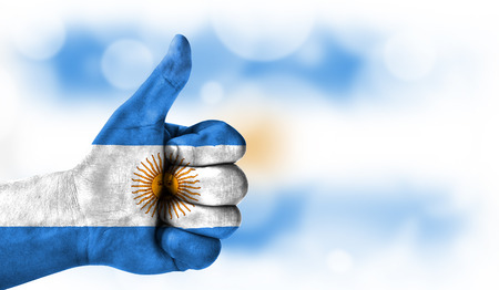 Flag of Argentina drawn on a man's hand with a thumb up, on a blurry background with a good place for textの写真素材