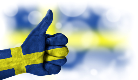 Flag of Sweden drawn on a man's hand with a thumb up, on a blurry background with a good place for textの写真素材