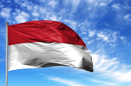 National flag of Indonesia on a flagpole in front of blue sky.の写真素材