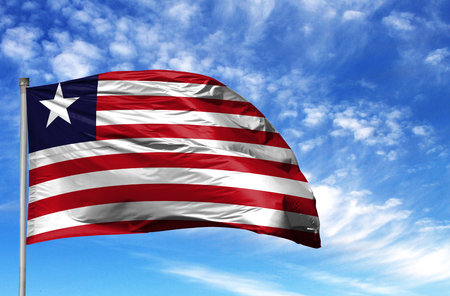 National flag of Liberia on a flagpole in front of blue sky.の写真素材