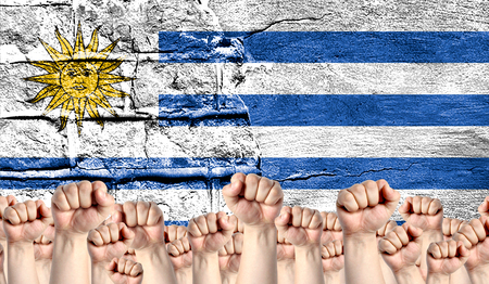 Male hands clenched in a fist raised up against the backdrop of a destroyed brick wall with a flag of Uruguay. The concept of the labor movement from the people, the power and strength of civil society.の写真素材
