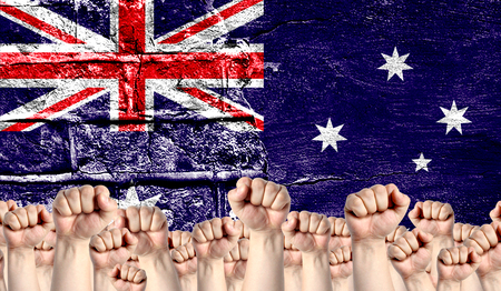Male hands clenched in a fist raised up against the backdrop of a destroyed brick wall with a flag of Australia. The concept of the labor movement from the people, the power and strength of civil society.の写真素材