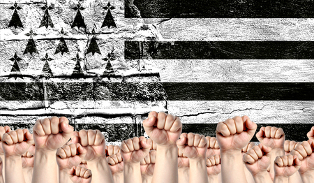 Male hands clenched in a fist raised up against the backdrop of a destroyed brick wall with a flag of Brittany. The concept of the labor movement from the people, the power and strength of civil society.の写真素材