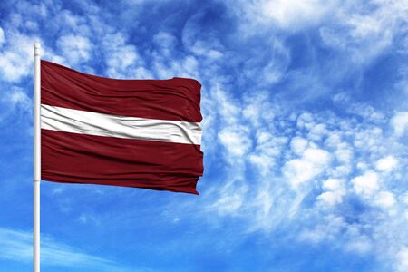 National flag of Latvia on a flagpole in front of blue skyの写真素材