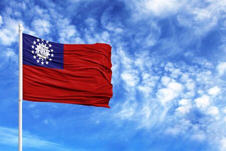 National flag of Myanmar Burma on a flagpole in front of blue skyの写真素材