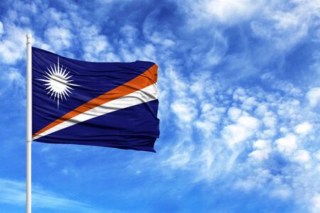 National flag of Marshall Islands on a flagpole in front of blue sky
