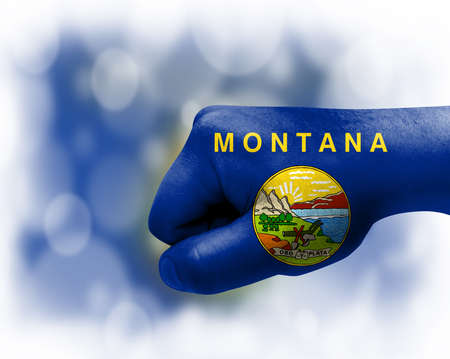 Flag of State of Montana painted on male fist, strength, power, concept of conflict. On a blurred background.の写真素材