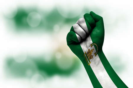 Flag of Andalusia painted on male fist, strength, power, concept of conflict. On a blurred background.の写真素材