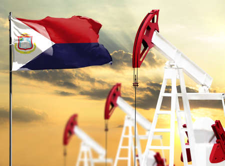 Oil rigs against the backdrop of the colorful sky and a flagpole with the flag of Saint Martin. The concept of oil production, minerals, development of new deposits.の写真素材