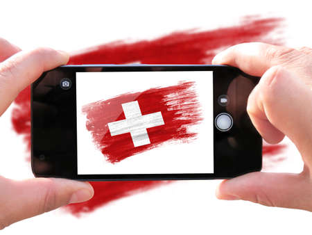 brush painted flag of Switzerland. The hands of men make a photo from the phone. Shooting from the smartphone.の写真素材