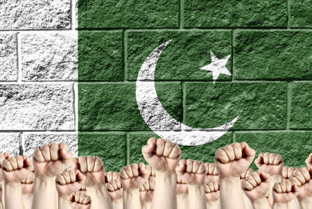 Raised fists against the background of the depicted flag of Pakistan on a brick wall, a concept of...