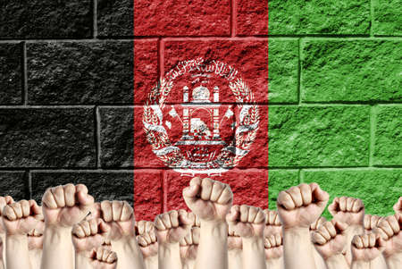 Raised fists against the background of the depicted flag of Afghanistan on a brick wall, a concept of strength and unity.の写真素材