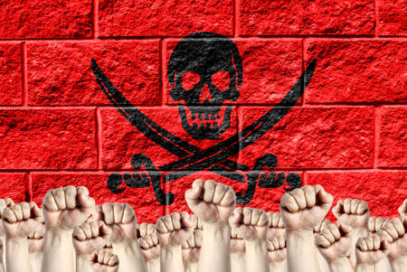 Raised fists against the background of the depicted flag of Pirates red on a brick wall, a concept of strength and unity.の写真素材