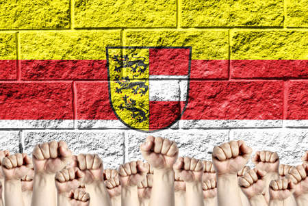 Raised fists against the background of the depicted flag of Carinthia on a brick wall, a concept of strength and unity.の写真素材
