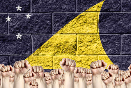 Raised fists against the background of the depicted flag of Tokelau on a brick wall, a concept of strength and unity.の写真素材