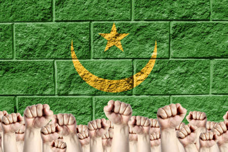 Raised fists against the background of the depicted flag of Mauritania on a brick wall, a concept of strength and unity.の写真素材