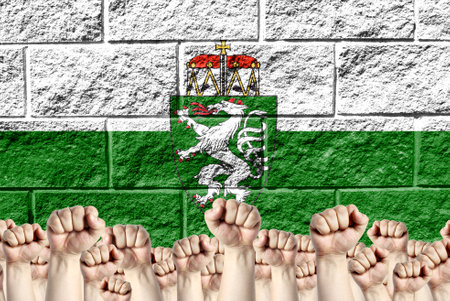 Raised fists against the background of the depicted flag of Styria on a brick wall, a concept of strength and unity.の写真素材