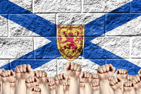 Raised fists against the background of the depicted flag of Nova Scotia on a brick wall, a concept of strength and unity.の写真素材