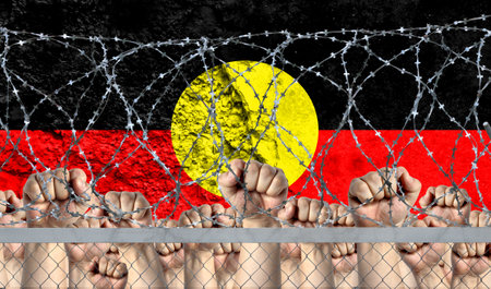 Raised fists against the background of the depicted flag of Australian Aboriginal behind barbed wire.の写真素材