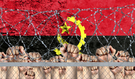 Raised fists against the background of the depicted flag of Angola behind barbed wire.