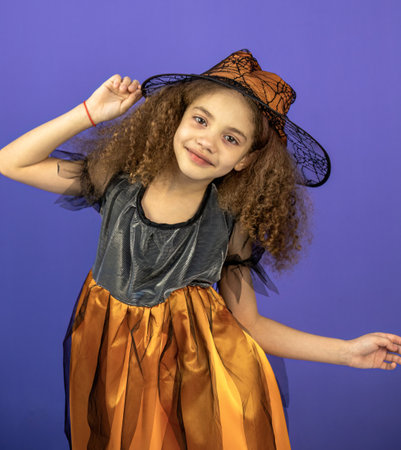 Little girl with curly hair in a witch costume on a purple backgroundの写真素材